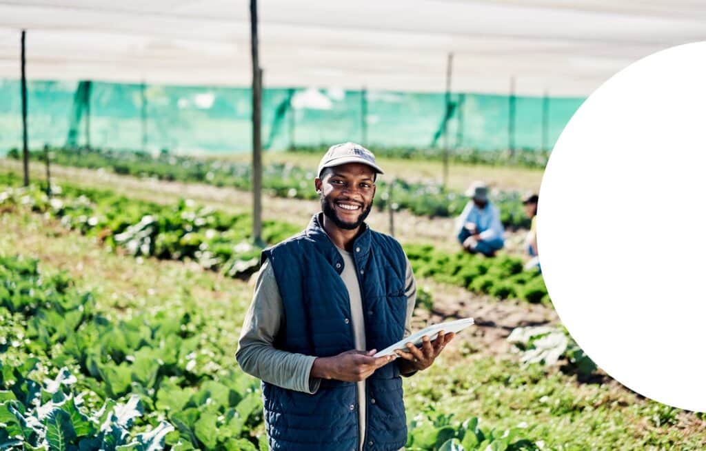 Portrait of happy young farmer using digital tablet while working on organic sustainable farm to cultivate vegetation in agribusiness. Man using technology to prepare harvest and monitor plant growth